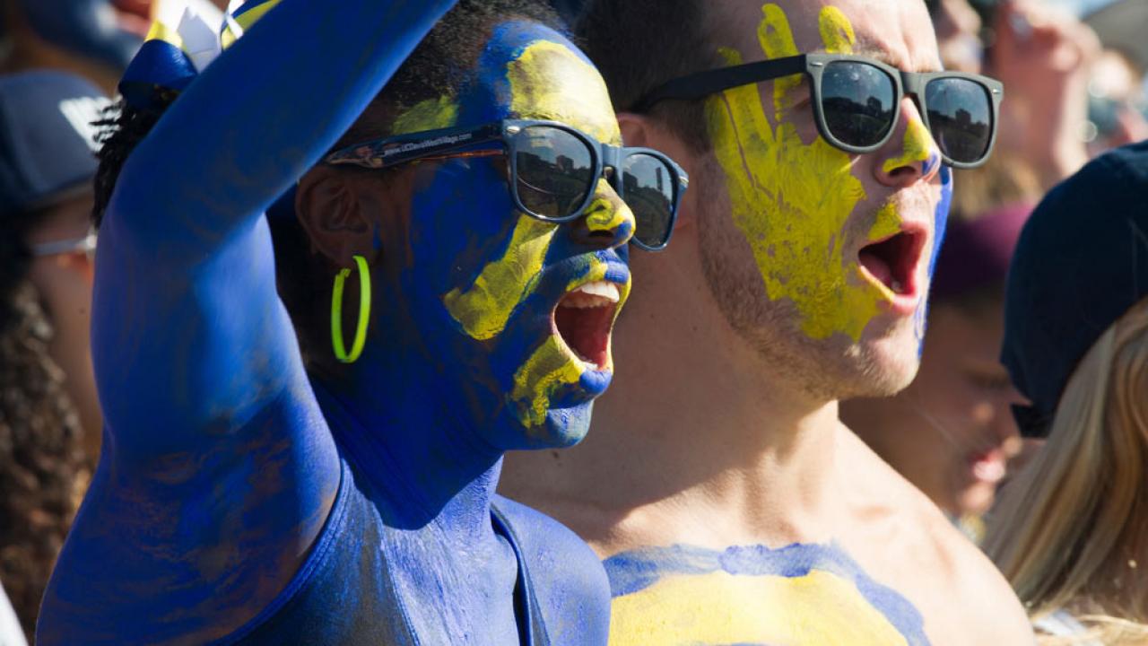 a male and female student painted in TV blue and gold cheer on the Aggies at the annual homecoming football game