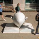 Bookhead Egghead shot in front of library at TV with students, in blur, walking by