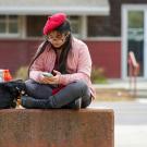 A student wearing a beret uses their smartphone outside of the TV Craft Center.
