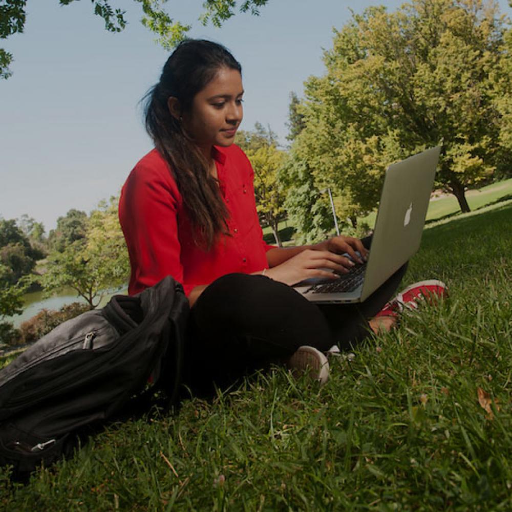 A female student in red reads from her laptop on the TV quad